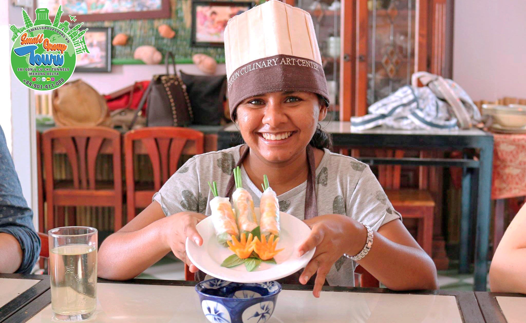 A delighted tourist proudly showcases her culinary masterpiece—a beautifully decorated Vietnamese fresh spring roll with an intricate carrot flower.